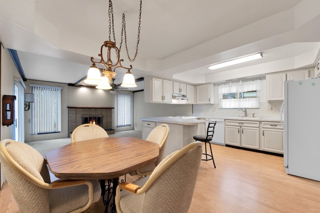 dining room featuring sink, a chandelier, a tray ceiling, a fireplace, and light hardwood / wood-style floors