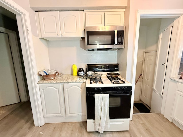 kitchen with white cabinetry, light stone counters, gas range oven, and light wood-type flooring