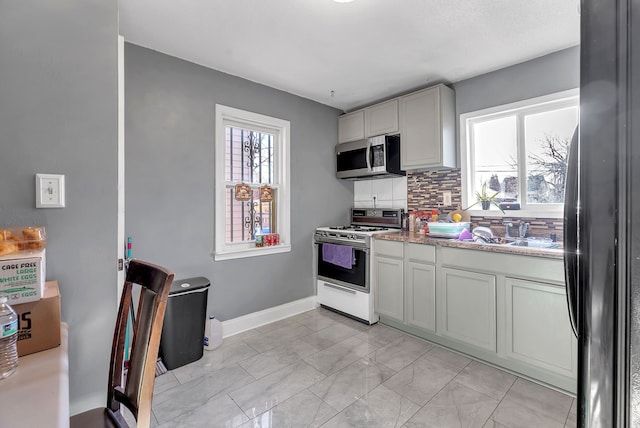 kitchen with tasteful backsplash, light stone countertops, white gas range, and sink