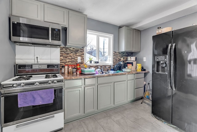 kitchen featuring gray cabinetry, decorative backsplash, black refrigerator with ice dispenser, and gas range gas stove