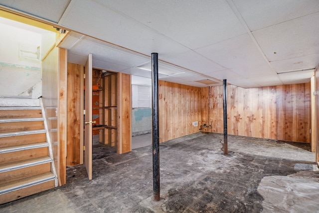 basement featuring a drop ceiling and wood walls