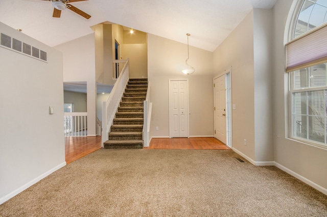 carpeted entryway with ceiling fan and high vaulted ceiling