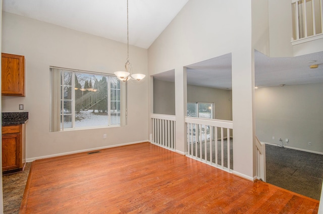 unfurnished dining area with hardwood / wood-style flooring, a notable chandelier, and high vaulted ceiling