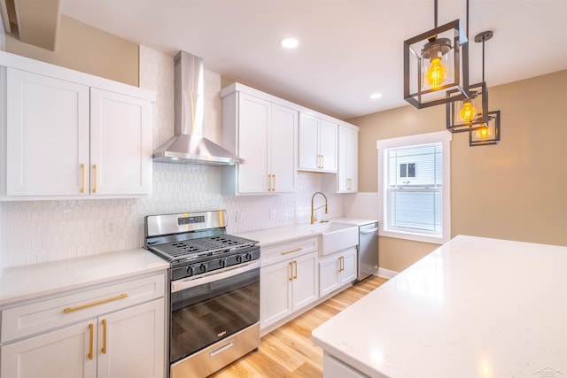 kitchen featuring light hardwood / wood-style flooring, appliances with stainless steel finishes, hanging light fixtures, white cabinets, and wall chimney exhaust hood