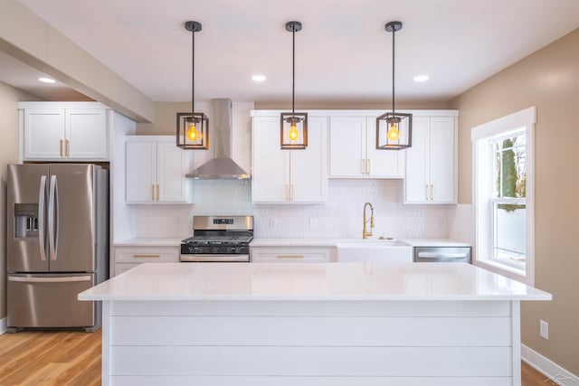 kitchen featuring wall chimney range hood, sink, white cabinetry, stainless steel appliances, and decorative light fixtures