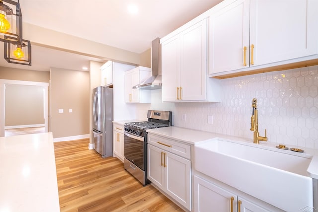 kitchen with wall chimney range hood, sink, appliances with stainless steel finishes, white cabinetry, and light hardwood / wood-style floors