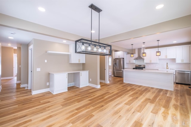 kitchen featuring wall chimney range hood, appliances with stainless steel finishes, white cabinetry, hanging light fixtures, and a kitchen island