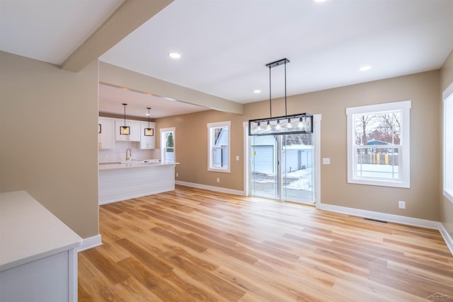 unfurnished living room featuring sink, beam ceiling, and light wood-type flooring