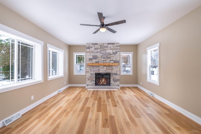 unfurnished living room featuring ceiling fan, a stone fireplace, and light hardwood / wood-style floors