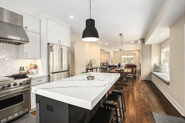 kitchen with decorative light fixtures, stainless steel appliances, a center island, and wall chimney exhaust hood