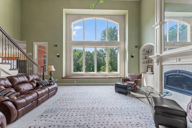 carpeted living room featuring a towering ceiling, a tile fireplace, and built in shelves