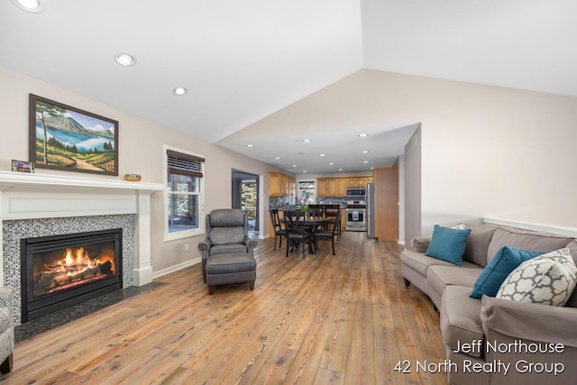 living room featuring a tiled fireplace, vaulted ceiling, and light hardwood / wood-style floors