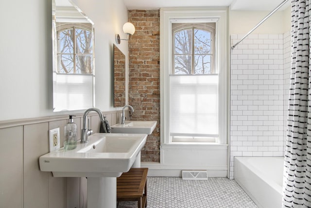 bathroom with shower / tub combo with curtain, a healthy amount of sunlight, and brick wall