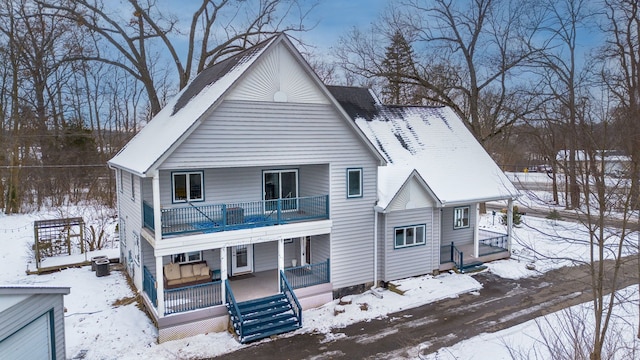 snow covered house featuring a porch and a balcony