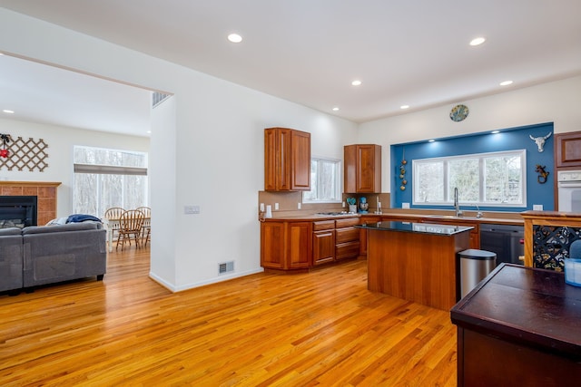 kitchen with sink, a tile fireplace, a center island, light hardwood / wood-style floors, and oven