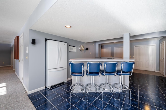 kitchen with white fridge, a breakfast bar, dark tile patterned flooring, and a textured ceiling