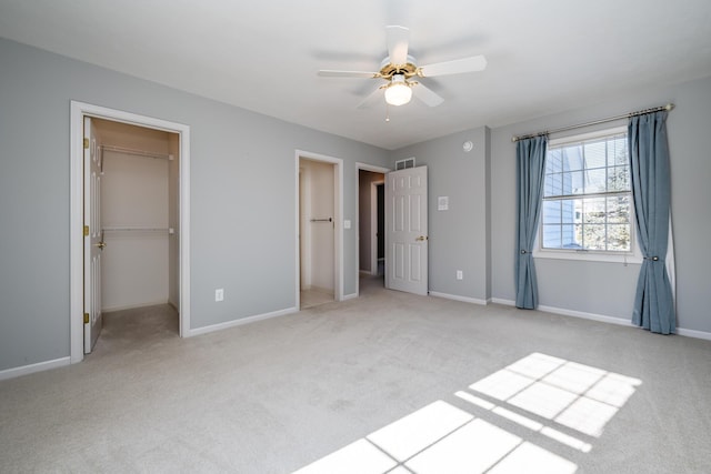 unfurnished bedroom featuring light carpet, a walk in closet, a closet, and ceiling fan