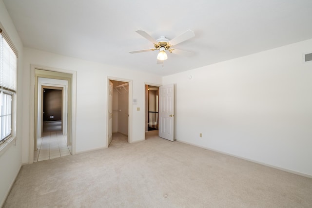 unfurnished bedroom featuring light carpet, a walk in closet, a closet, and ceiling fan