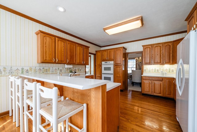 kitchen featuring a breakfast bar, crown molding, wood-type flooring, kitchen peninsula, and white appliances