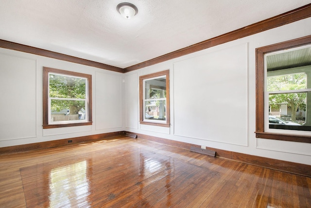 spare room with wood-type flooring, ornamental molding, and a textured ceiling