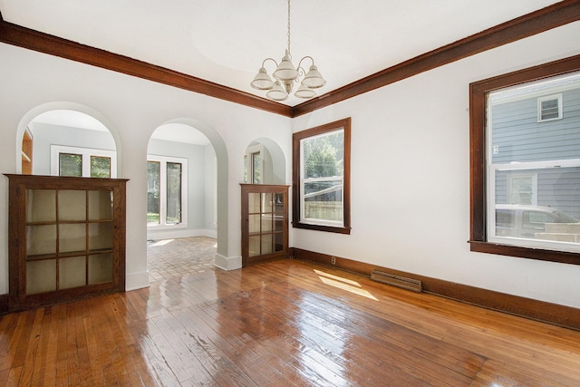 empty room featuring hardwood / wood-style flooring, ornamental molding, and a chandelier