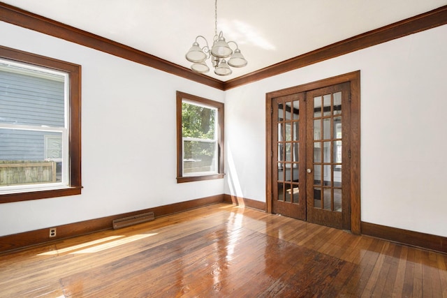 empty room with hardwood / wood-style floors, crown molding, a notable chandelier, and french doors