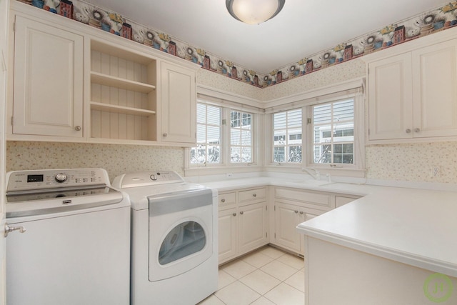 clothes washing area with light tile patterned floors, sink, washing machine and dryer, and cabinets