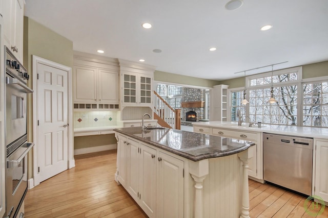 kitchen featuring stainless steel appliances, a stone fireplace, a center island with sink, and decorative light fixtures