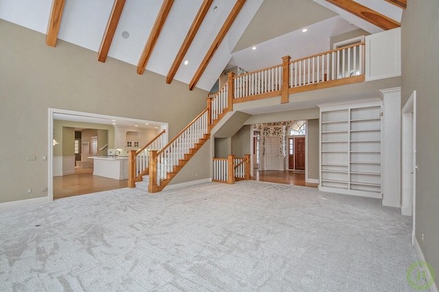 unfurnished living room featuring light colored carpet, beam ceiling, and high vaulted ceiling