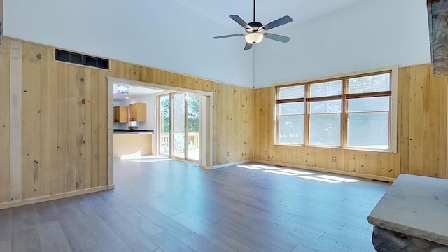 unfurnished living room featuring hardwood / wood-style flooring, ceiling fan, wooden walls, and high vaulted ceiling