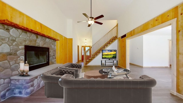 living room with a stone fireplace, a towering ceiling, ceiling fan, and hardwood / wood-style flooring