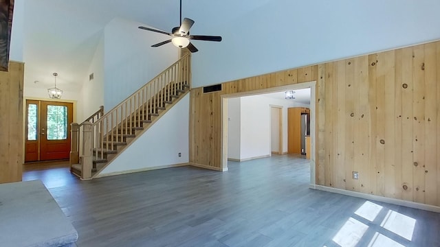 unfurnished living room featuring hardwood / wood-style flooring, a high ceiling, ceiling fan, and wood walls