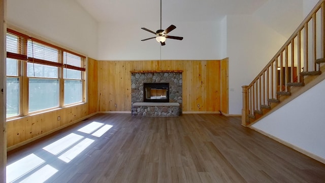 unfurnished living room featuring a towering ceiling, hardwood / wood-style floors, a fireplace, and wood walls