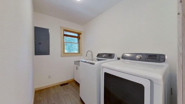 clothes washing area with electric panel, washing machine and dryer, and light hardwood / wood-style flooring