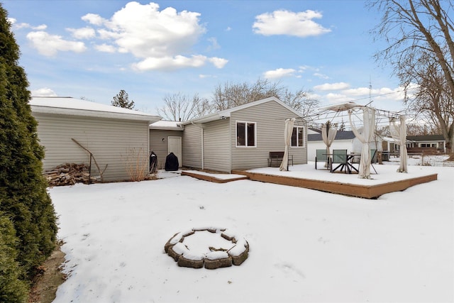 snow covered house featuring a wooden deck and a fire pit