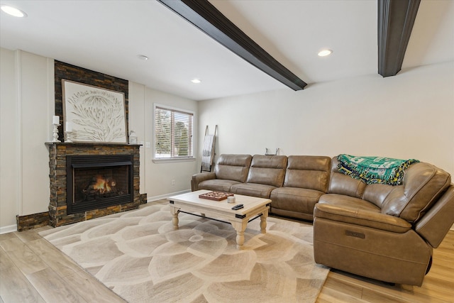 living room featuring a stone fireplace, light hardwood / wood-style flooring, and beamed ceiling