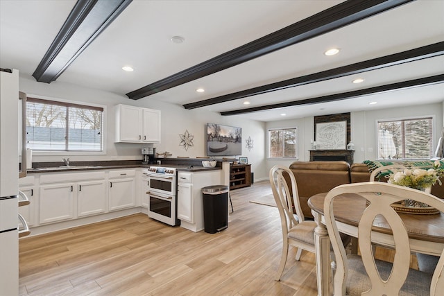 kitchen with beamed ceiling, white cabinetry, double oven range, light hardwood / wood-style floors, and kitchen peninsula