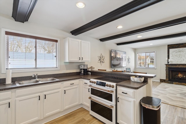 kitchen featuring sink, kitchen peninsula, beam ceiling, range with two ovens, and white cabinets