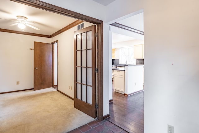 corridor with dark colored carpet, visible vents, crown molding, and baseboards