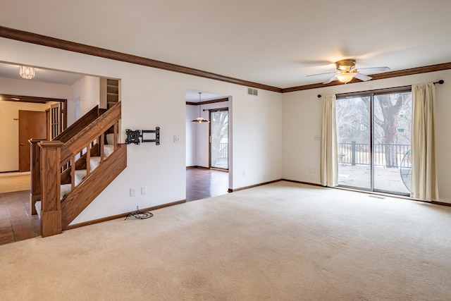 carpeted empty room featuring ceiling fan, visible vents, baseboards, ornamental molding, and stairway