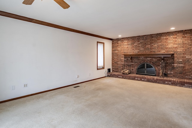 unfurnished living room with carpet floors, crown molding, a ceiling fan, a brick fireplace, and baseboards