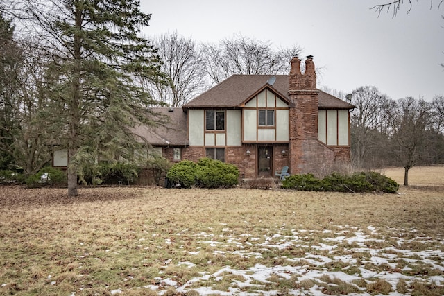 tudor house featuring a shingled roof, brick siding, a chimney, and stucco siding