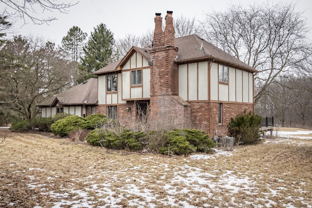 snow covered property featuring brick siding, a chimney, a shingled roof, and stucco siding