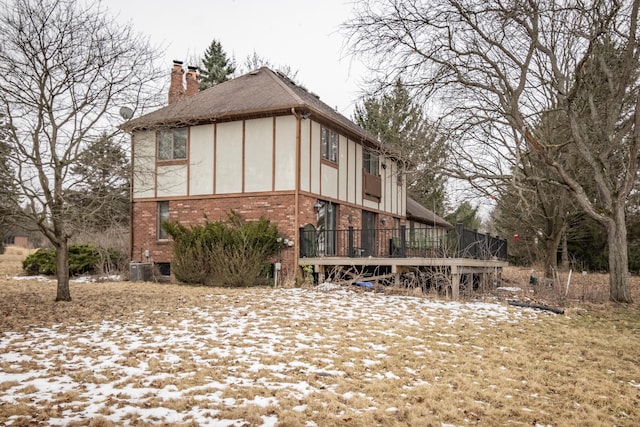 snow covered property with stucco siding, a chimney, a deck, and brick siding