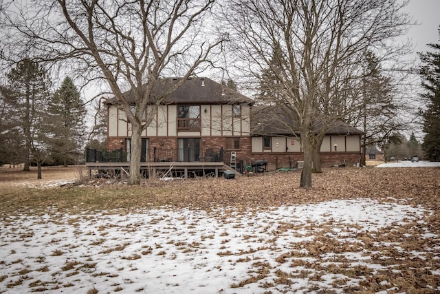 snow covered rear of property with brick siding and a deck