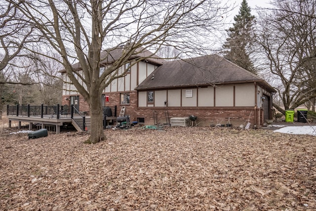 view of property exterior with a garage, brick siding, roof with shingles, a wooden deck, and stucco siding