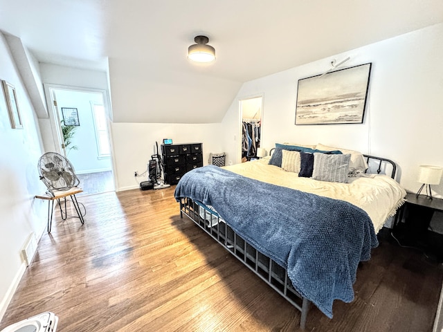 bedroom with wood-type flooring, a spacious closet, vaulted ceiling, and a closet