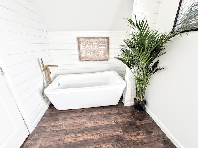 bathroom with hardwood / wood-style flooring, lofted ceiling, wooden walls, and a tub