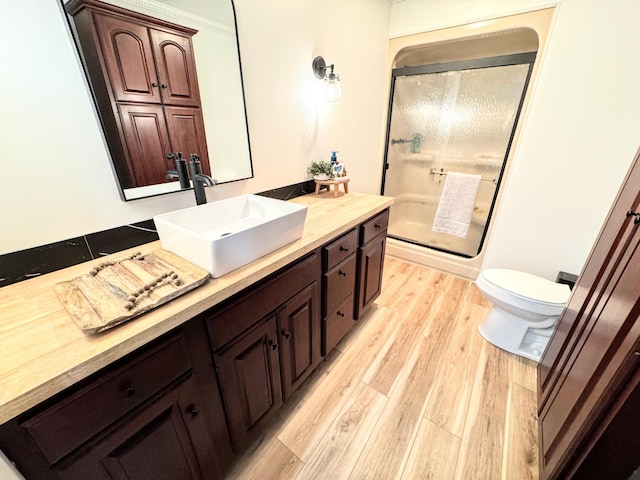 bathroom featuring wood-type flooring, toilet, vanity, and a shower with shower door