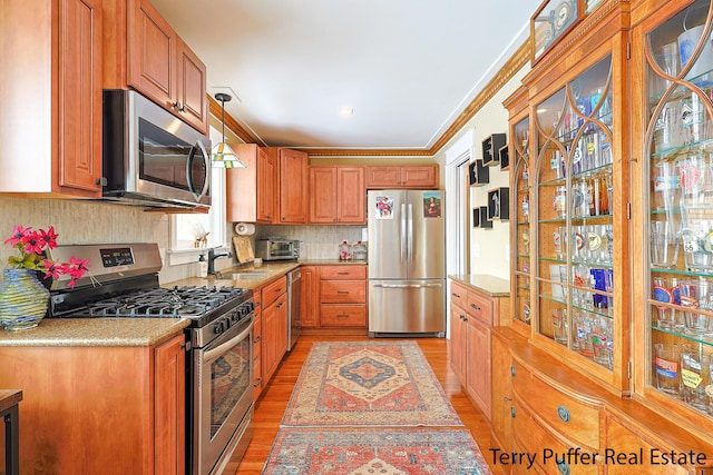 kitchen with crown molding, backsplash, stainless steel appliances, decorative light fixtures, and light wood-type flooring